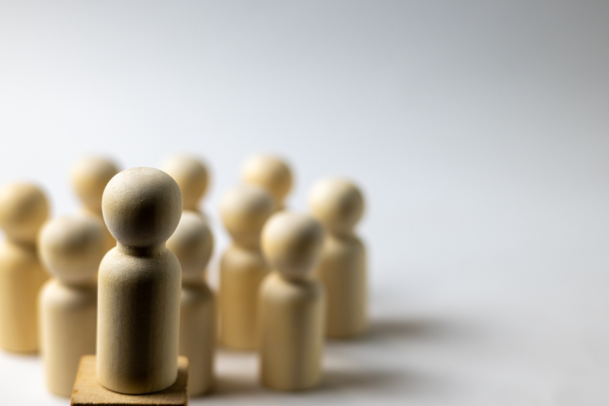 Eine einzelne Holzfigur steht mit Abstand vor einer Gruppe – Symbolbild für professionelle Nähe und Distanz