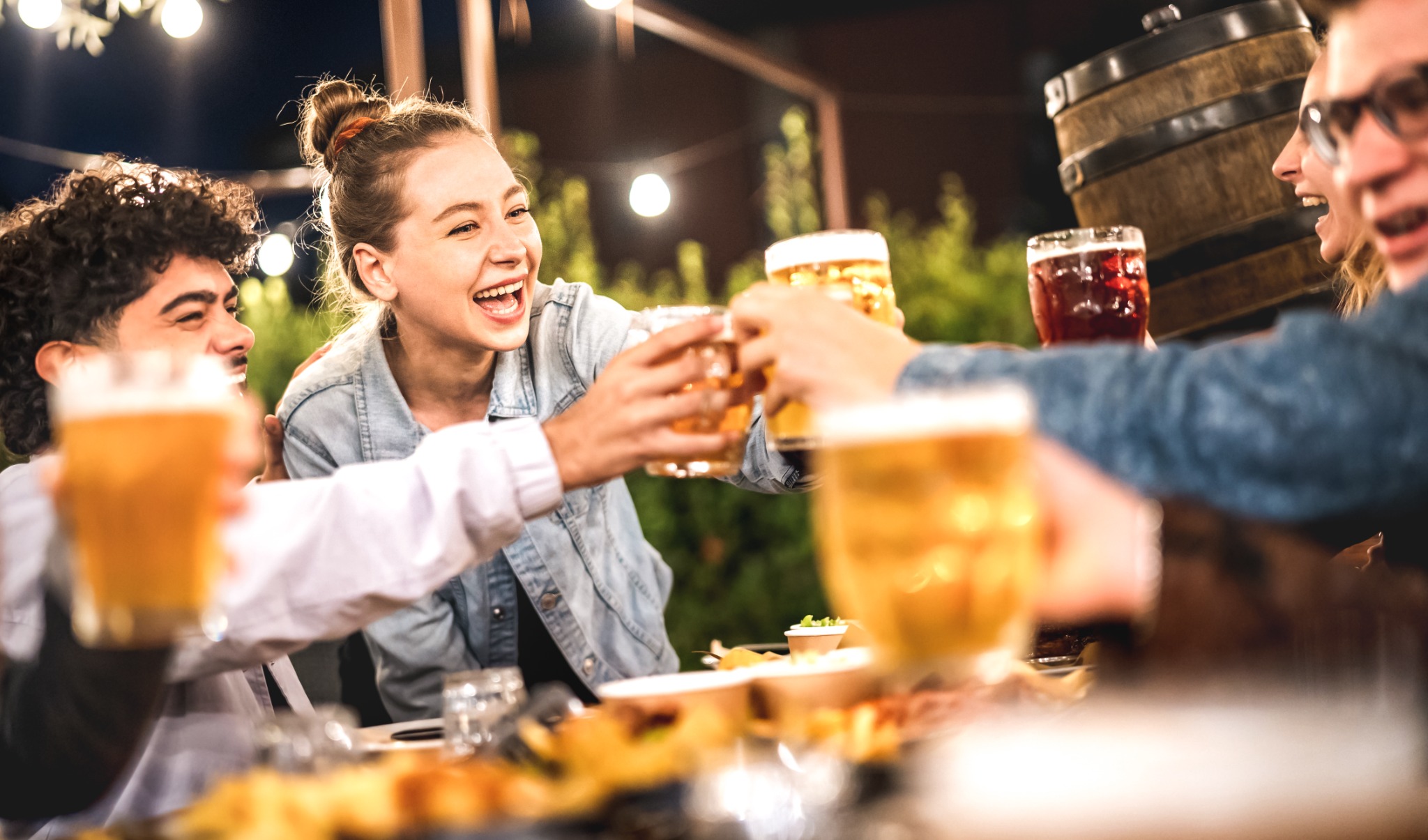 Menschen stoßen beim gemeinsamen Essen und Trinken im Außenbereich einer Gastronomie an